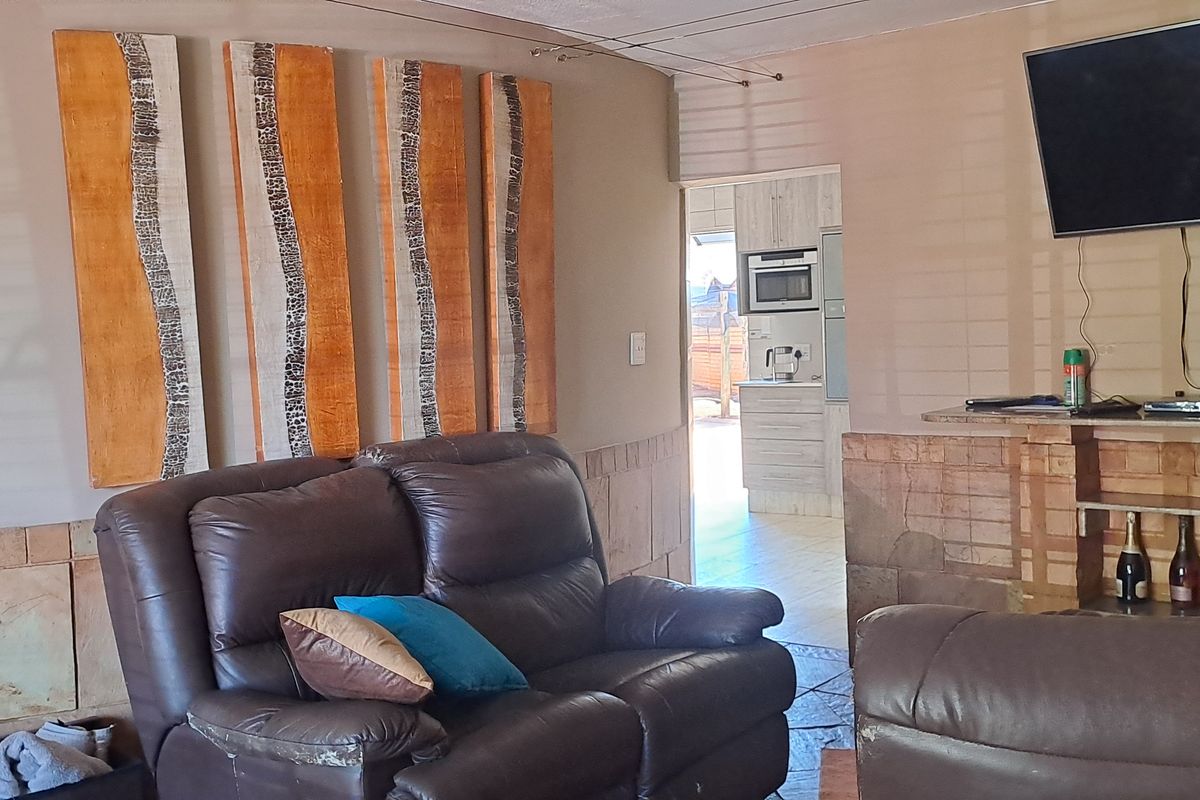 A living room featuring tiled wall accents and a built-in display unit, with a view through to the kitchen area.
