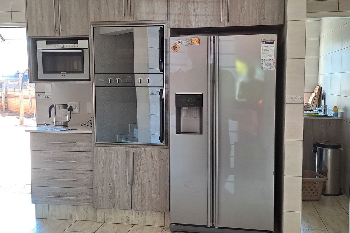 A functional kitchen featuring wood-grain cabinetry, built-in oven, microwave, and tiled flooring, with an adjacent scullery area visible.