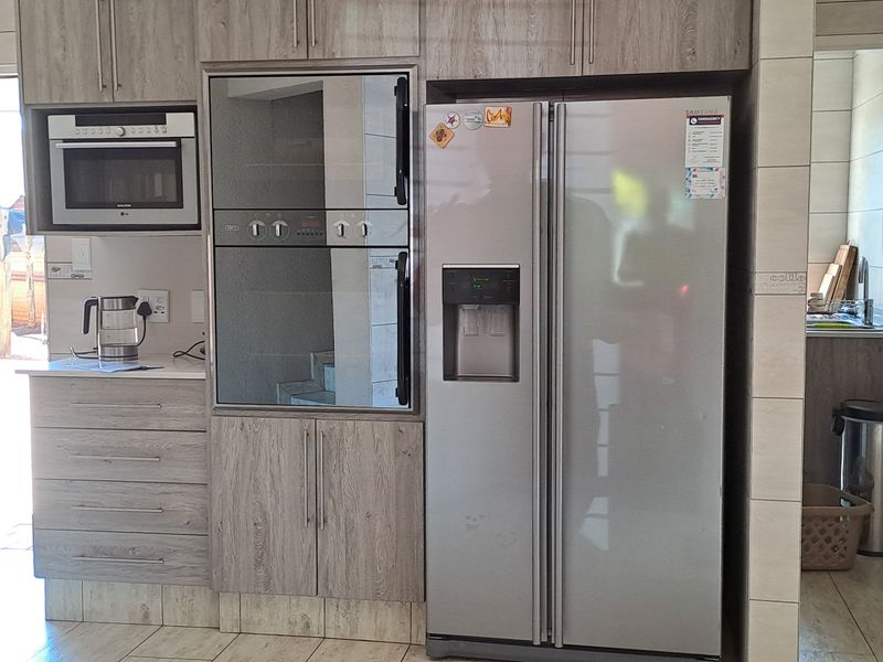 A functional kitchen featuring wood-look cabinetry, built-in oven and microwave, and tiled finishes, with an adjacent scullery area visible.