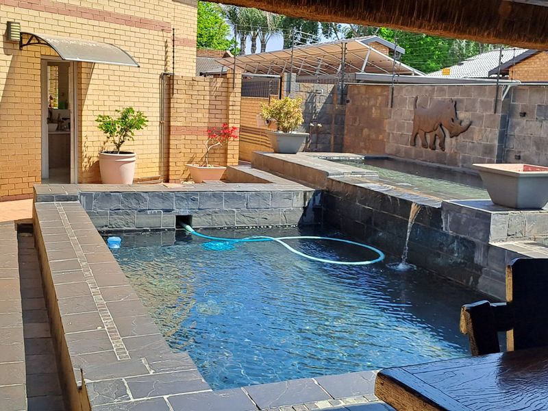 A well-maintained outdoor pool area featuring stone-clad walls, a built-in water feature, and a covered patio space.