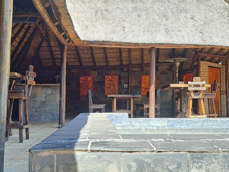 A spacious covered patio featuring a traditional thatched roof, stone-clad walls, and a built-in bar area, ideal for outdoor entertaining.