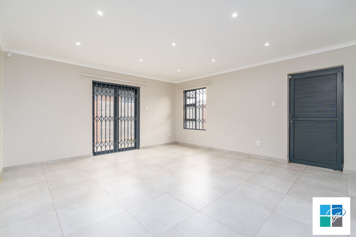 A bright, open-plan living area featuring neutral tiled flooring, recessed ceiling lighting, and secure metal security gates on the door and window.