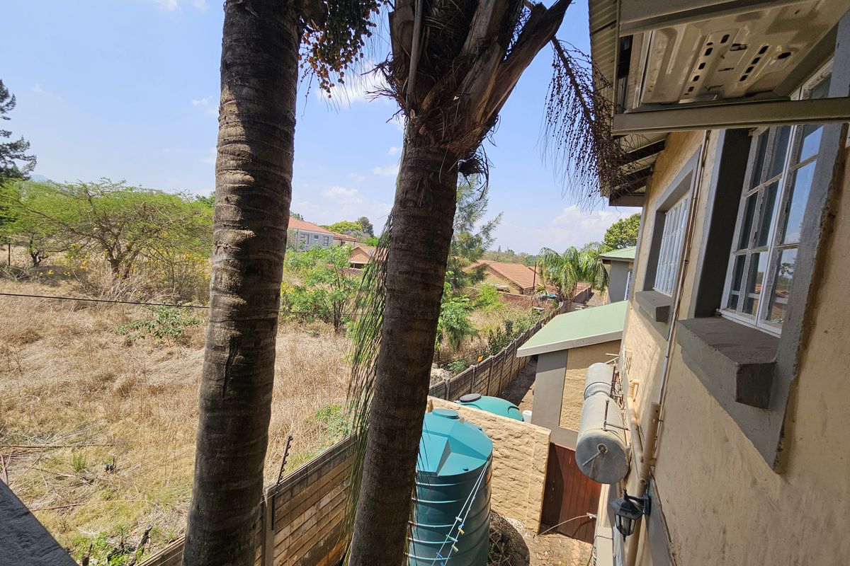 Rear exterior view of the property featuring a water storage tank, boundary wall with electric fencing, and mature palm trees.