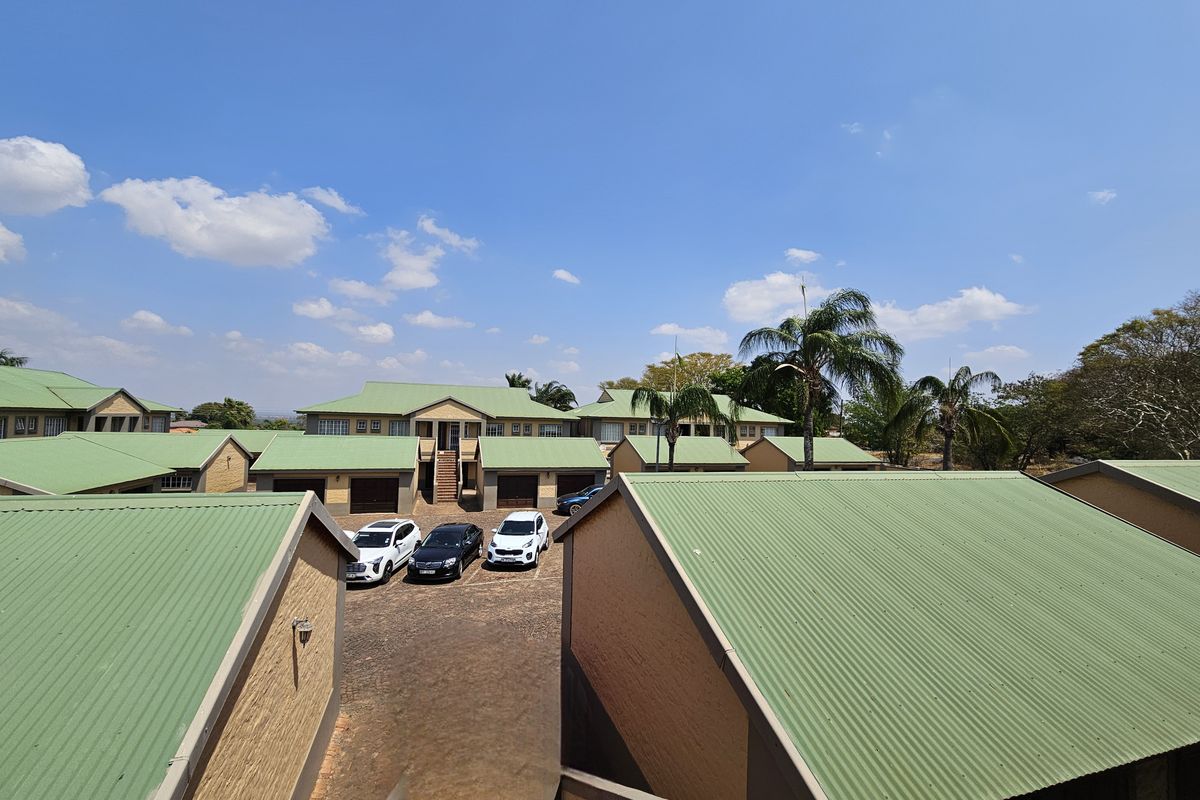 An elevated aerial view of a residential apartment complex featuring multiple units with green corrugated metal roofs and a central paved courtyard area.