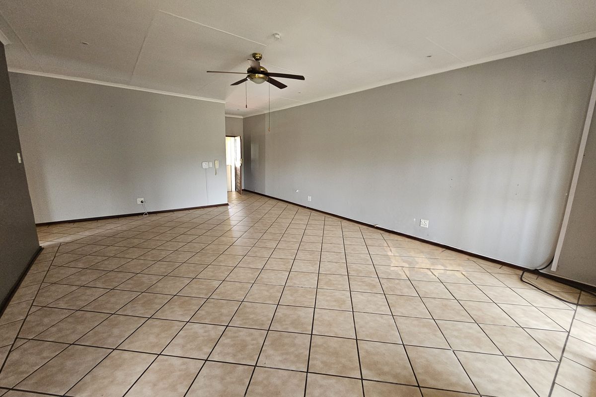 A spacious, empty living area featuring neutral grey walls, tiled flooring, and a central ceiling fan, offering a blank canvas for interior design.