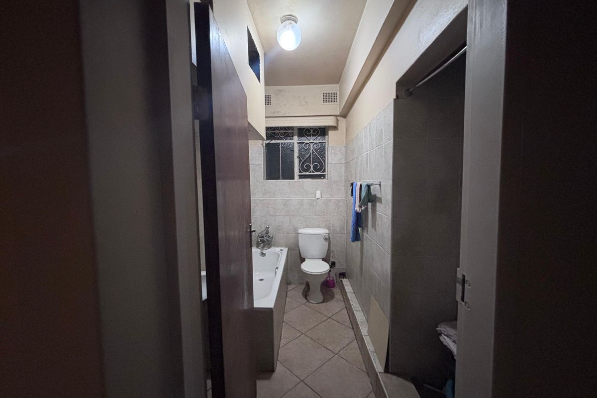 A functional bathroom featuring a bathtub, toilet, and tiled finishes, requiring cosmetic updates to improve its overall condition and aesthetic appeal.