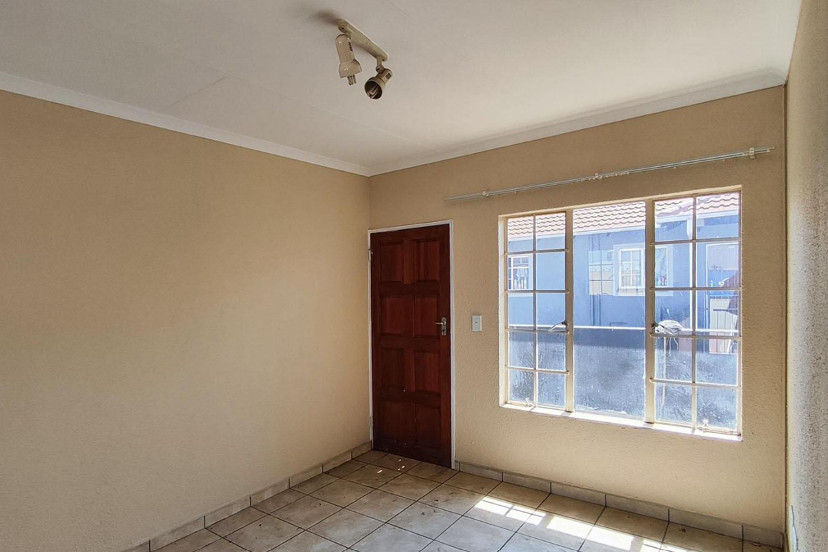 An empty bedroom featuring tiled flooring, a wooden door, and a window with security bars, offering a blank canvas for potential updates.
