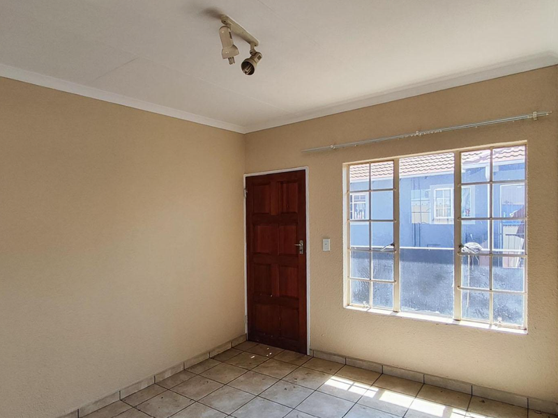 An empty bedroom featuring tiled flooring, a wooden door, and a window with security bars, offering a blank canvas for potential updates.