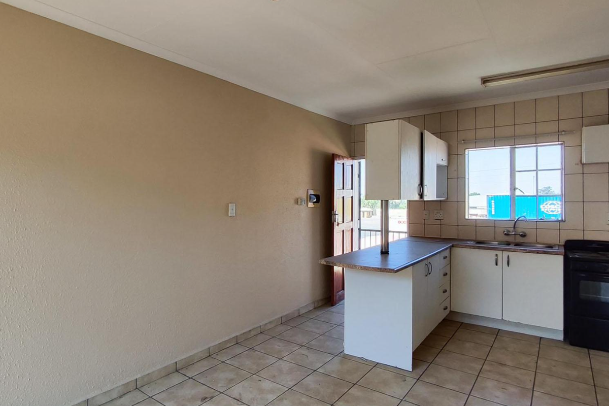 A functional kitchen featuring built-in cabinetry, laminate countertops, a stainless steel sink, and a freestanding stove with tiled backsplash and flooring.