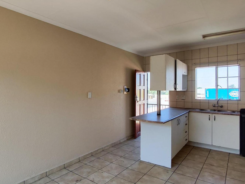 A functional kitchen featuring built-in cabinetry, laminate countertops, a stainless steel sink, and a freestanding stove with tiled backsplash and flooring.