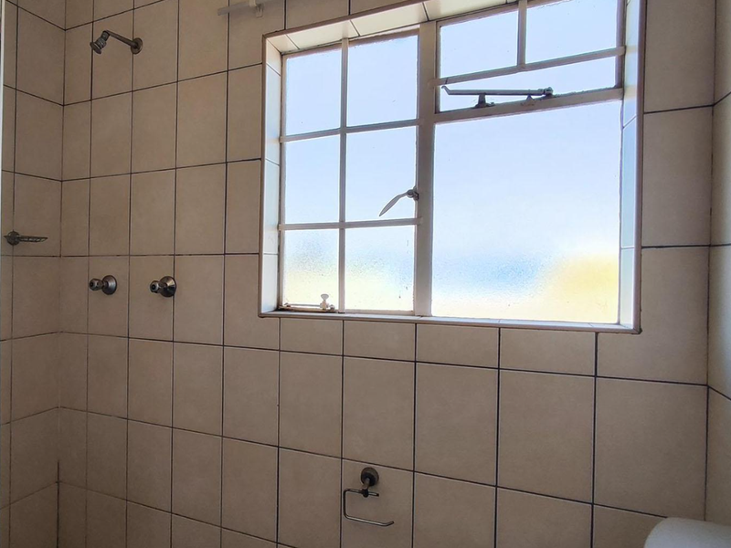 A dated bathroom shower area featuring tiled walls, a window, and basic plumbing fixtures, requiring cosmetic updates to improve its overall condition.