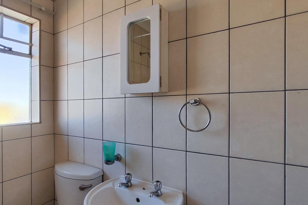 A functional bathroom featuring tiled walls, a pedestal basin with dual-handle mixer, a wall-mounted medicine cabinet, and a standard toilet.