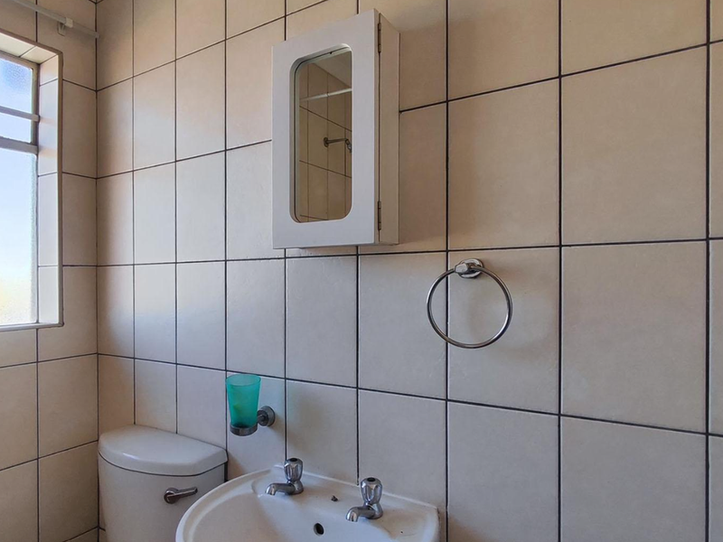 A functional bathroom featuring tiled walls, a pedestal basin with dual-handle mixer, a wall-mounted medicine cabinet, and a standard toilet.