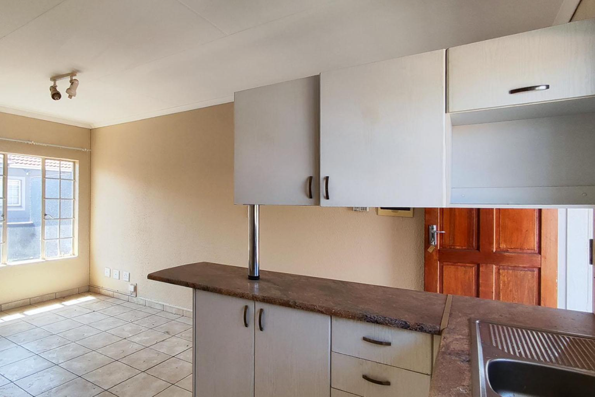 Open plan kitchen and living area featuring laminate cabinetry, stone-look countertops, stainless steel sink, and ceramic tiled flooring in a vacant apartment setting.