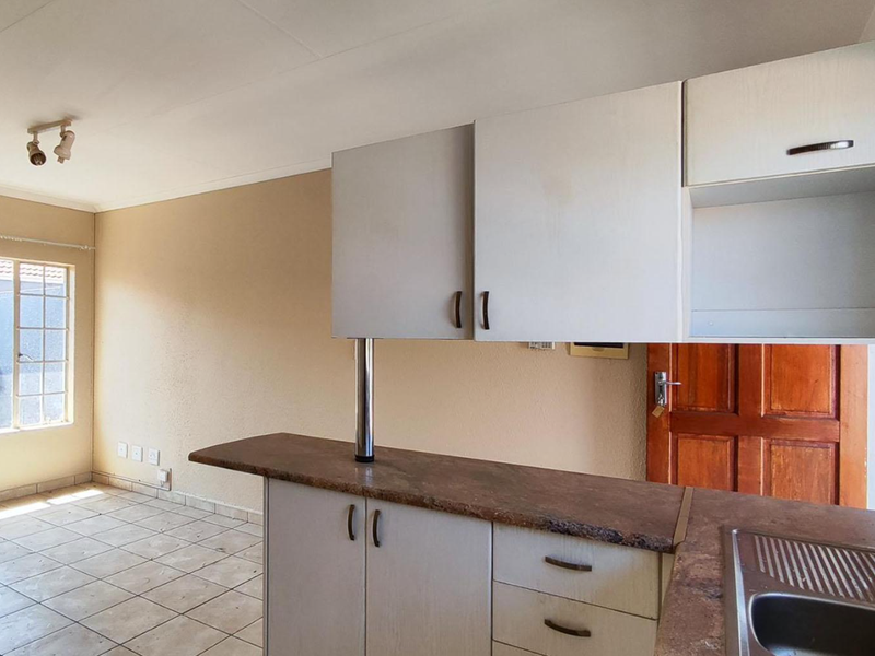 Open plan kitchen and living area featuring laminate cabinetry, stone-look countertops, stainless steel sink, and ceramic tiled flooring in a vacant apartment setting.