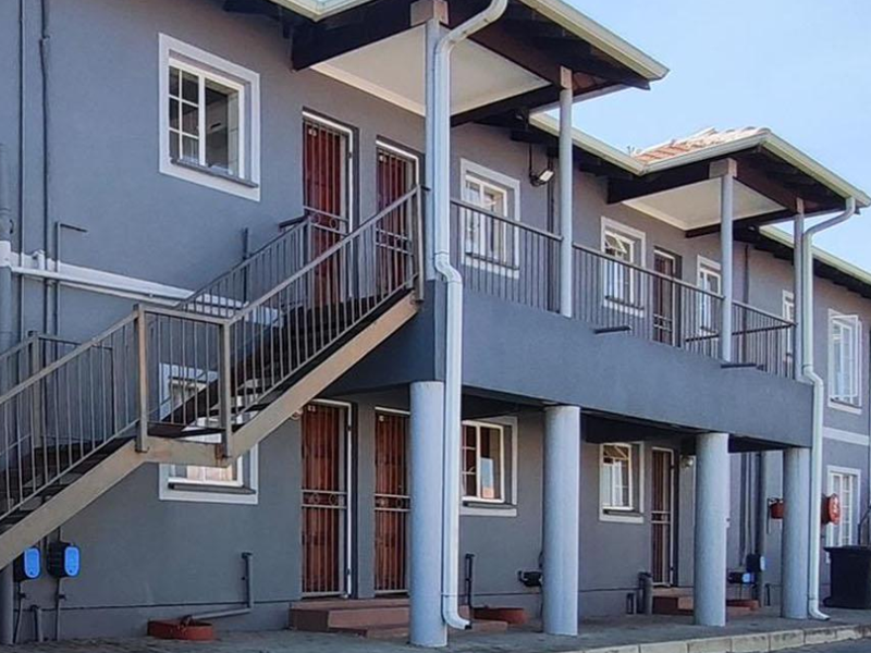Exterior view of a multi-story apartment complex featuring metal staircases, balconies, and security gates on the ground and upper levels.