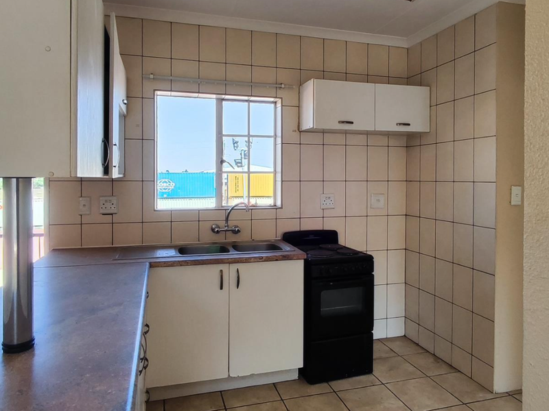 A functional kitchen featuring tiled splashbacks, laminate countertops, a double basin sink, and a freestanding stove with overhead and under-counter cabinetry.