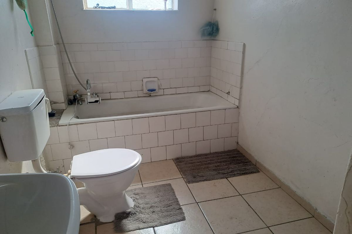 A dated bathroom featuring a standard bathtub, toilet, and tiled finishes, requiring cosmetic updates to improve its overall condition and appeal.