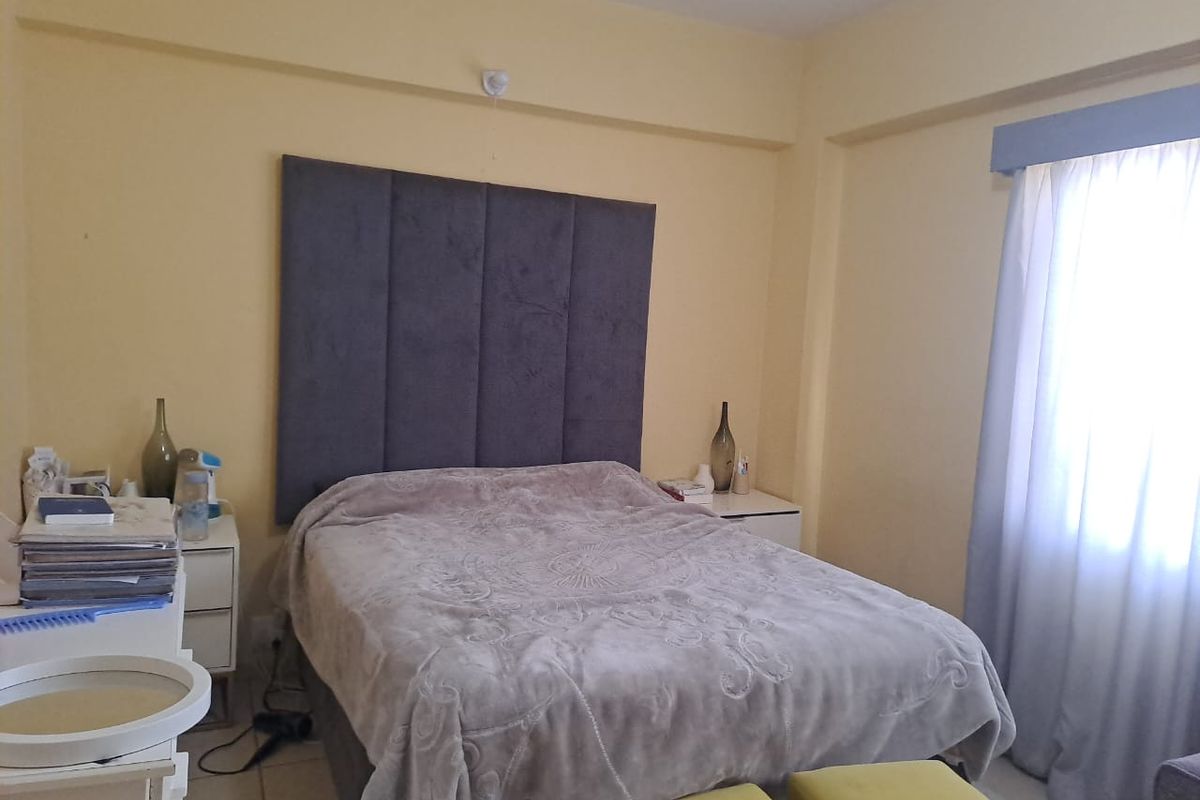 A functional bedroom featuring a large upholstered headboard, tiled flooring, and window treatments, offering a comfortable and neutral living space.