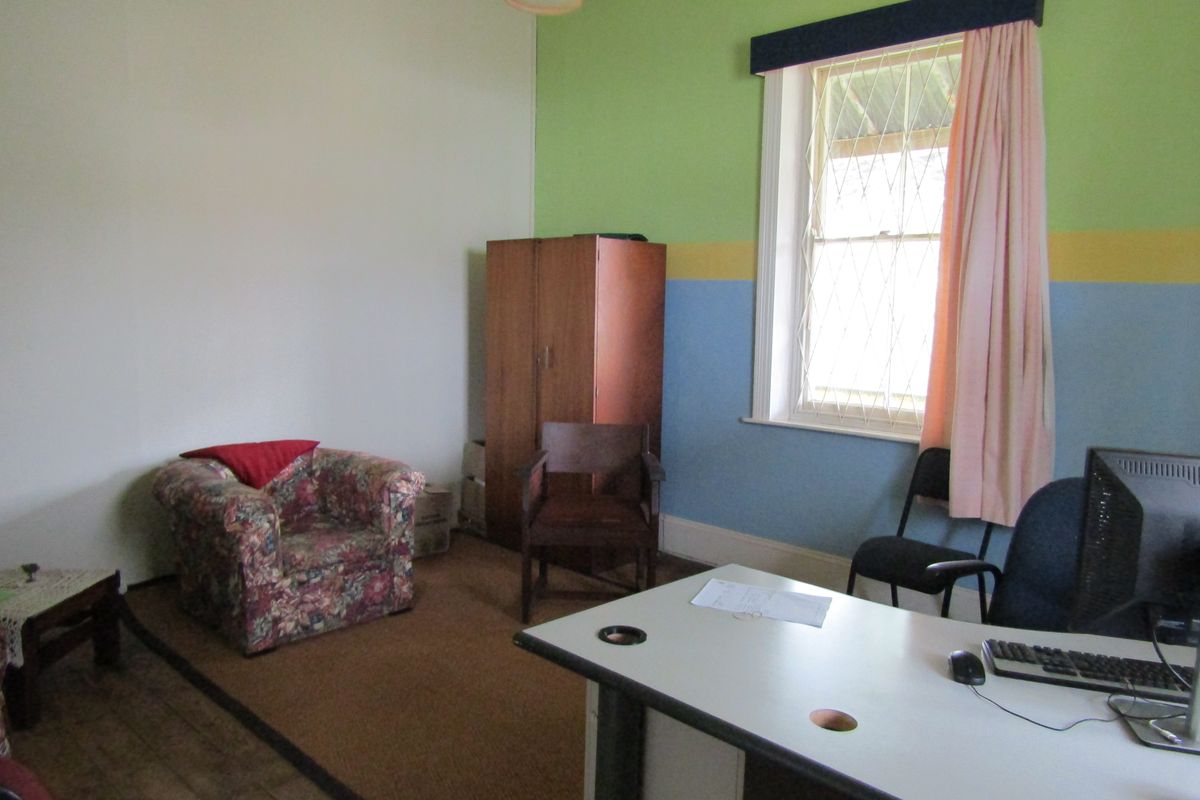 A multi-purpose room featuring a large window with security bars, neutral flooring, and multi-colored painted walls, suitable for use as a home office or bedroom.