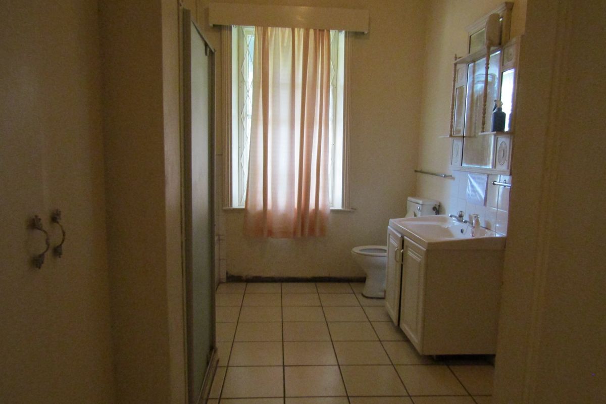 A dated bathroom featuring a vanity unit, toilet, and shower enclosure with tiled flooring and a window.