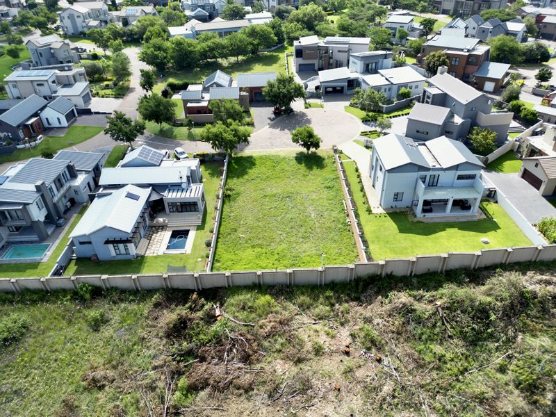 An aerial view of a vacant residential plot situated within a developed estate, featuring established boundary walls and surrounding modern homes.