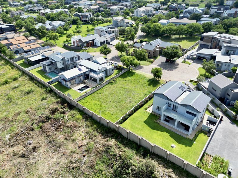 Aerial view of a residential estate featuring a vacant plot of land surrounded by established homes and perimeter fencing.