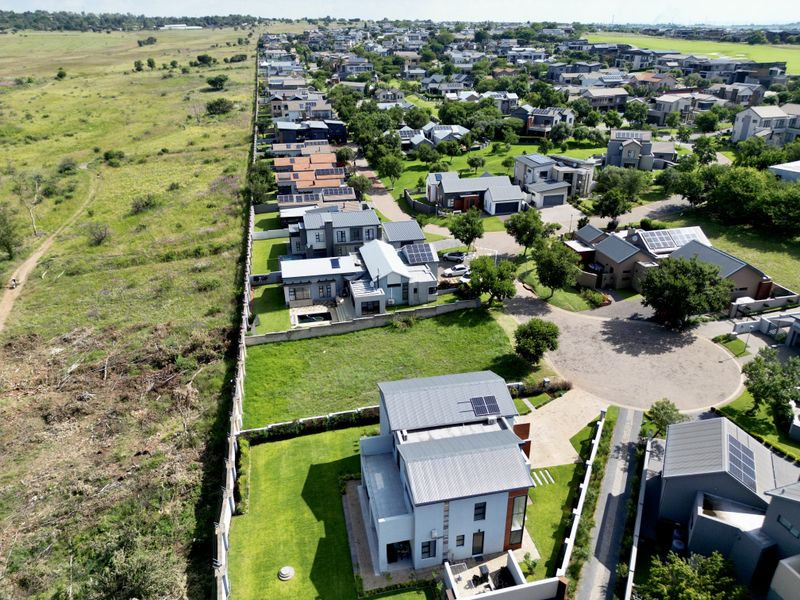 Aerial view of a residential property in a modern estate, featuring a well-maintained lawn, solar panels, and proximity to open green space.