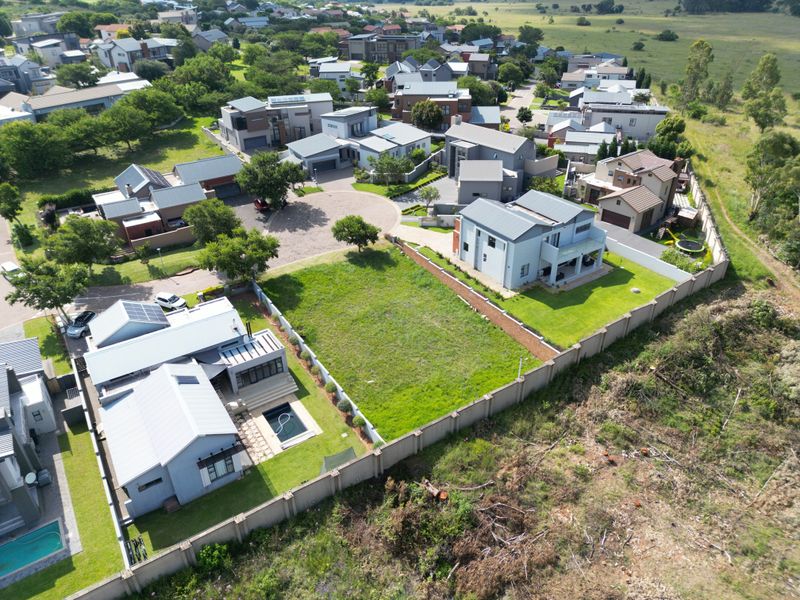 Aerial view of a vacant residential plot situated within a developed estate, featuring established perimeter walls and surrounding residential properties.