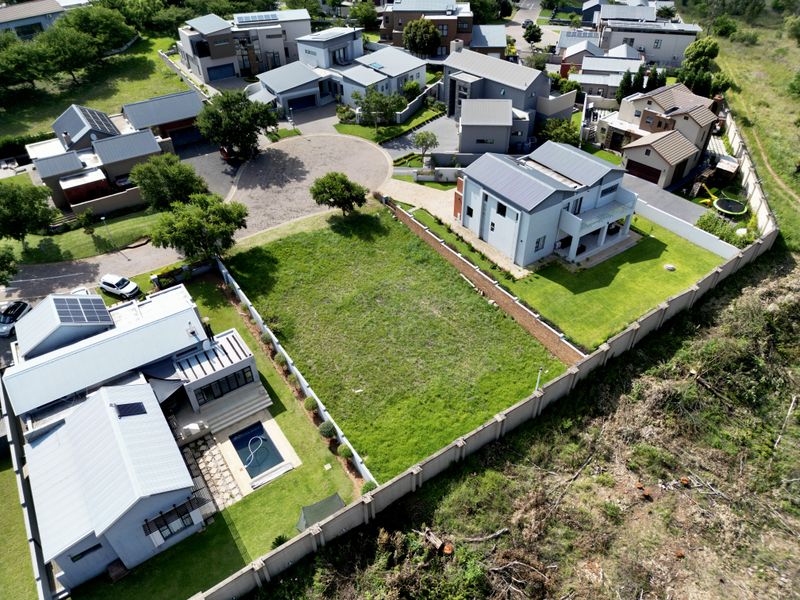 Aerial view of a vacant residential plot situated within a developed estate, featuring established boundary walls and surrounding modern residential properties.