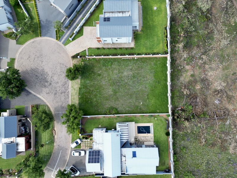 Aerial view of a vacant residential plot situated within a developed estate, featuring established boundary walls and surrounding landscaped grounds.