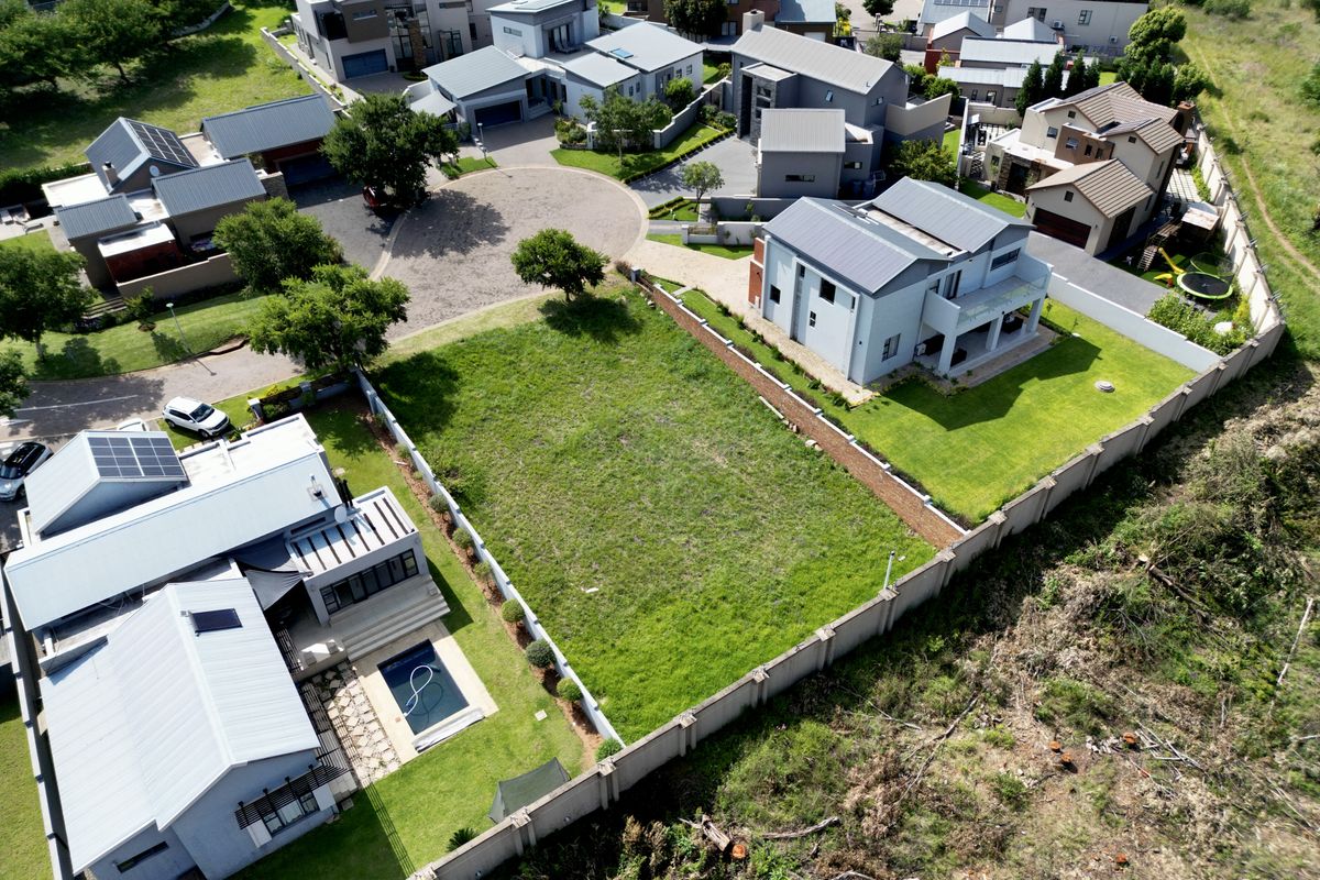 Aerial view of a vacant residential plot situated within a developed estate, featuring established boundary walls and surrounding modern residential properties.