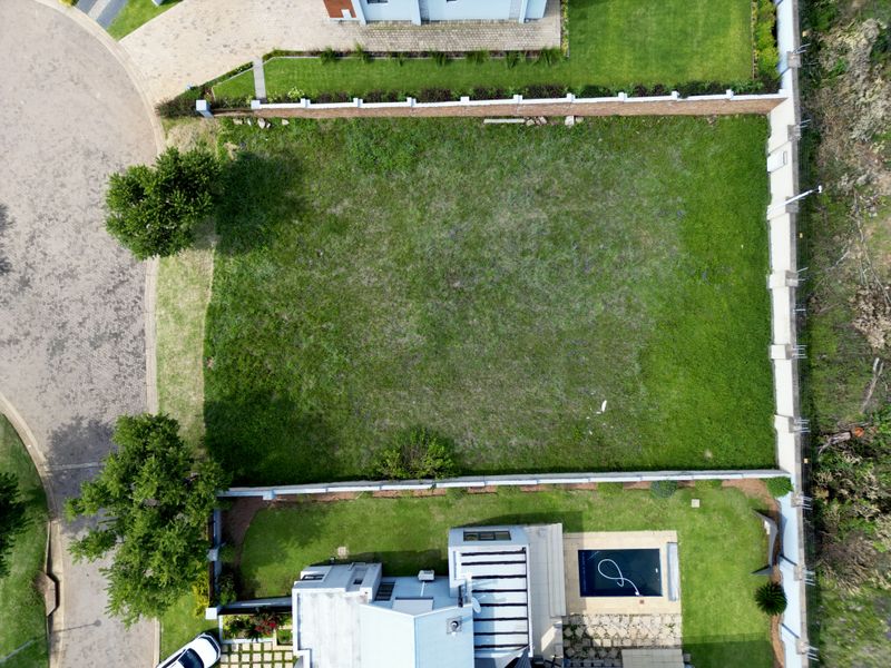 Aerial view of a vacant residential plot featuring a level grassed area, enclosed by boundary walls, situated adjacent to a paved street.
