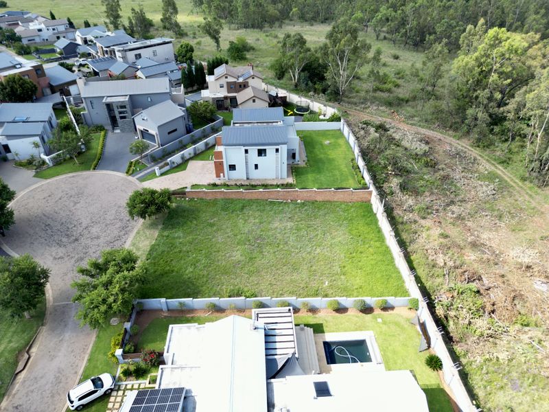Aerial view of a vacant residential plot situated within a developed estate, featuring established perimeter walls and surrounding green space.
