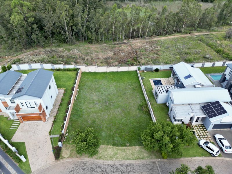 Aerial view of a vacant residential plot situated between two existing modern homes, featuring established perimeter walls and a level grassed area.