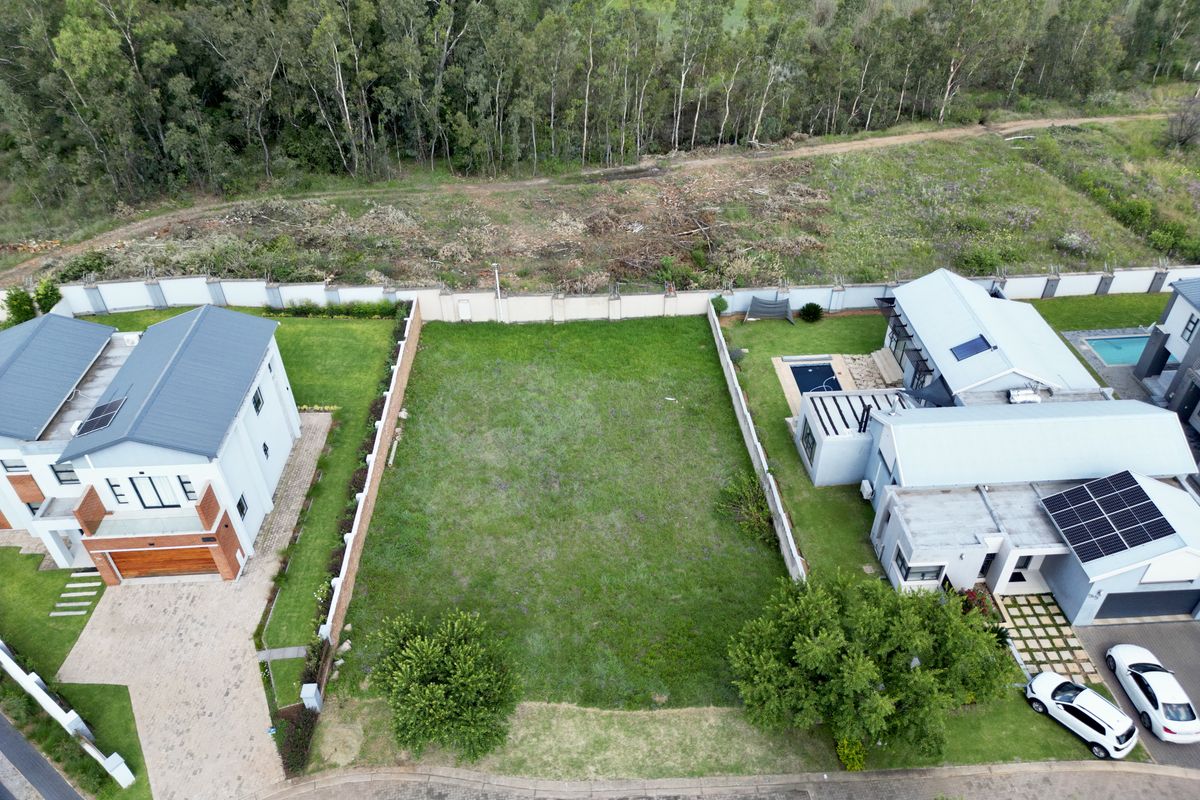 Aerial view of a vacant residential plot situated between two existing modern homes, featuring established perimeter walls and a level grassed area.