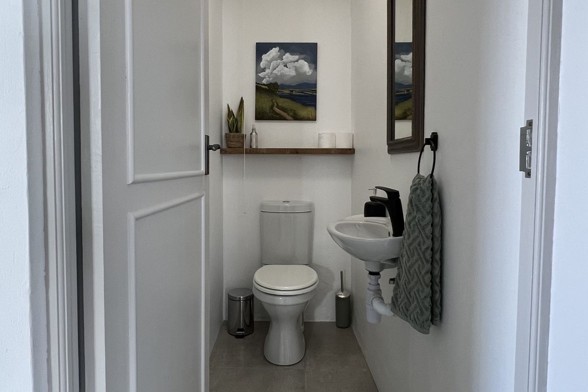 A compact guest bathroom featuring a wall-mounted basin, modern toilet, and neutral tiled flooring with clean white finishes.
