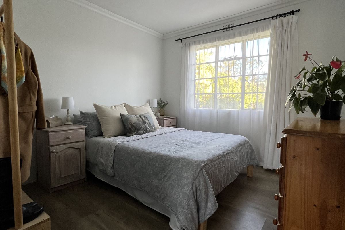 A well-maintained bedroom featuring laminate flooring, neutral walls, and a large window with security bars, providing natural light and a pleasant outlook.