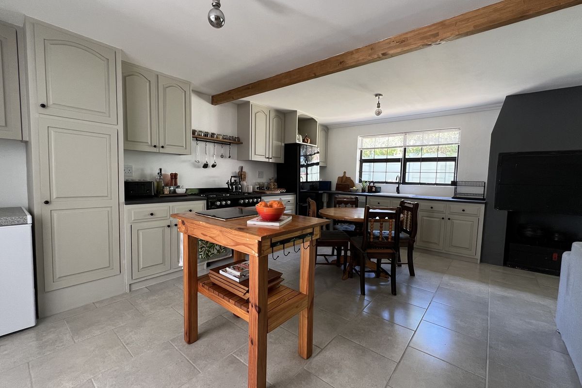 A spacious kitchen featuring light-toned cabinetry, tiled flooring, an exposed timber ceiling beam, and a built-in fireplace, offering a functional and warm cooking environment.