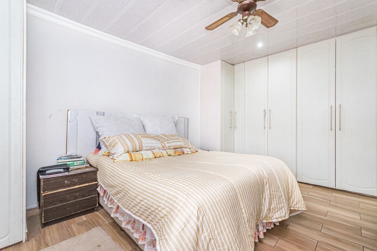 A bedroom featuring built-in floor-to-ceiling wardrobes, wood-look tiled flooring, and a ceiling fan.