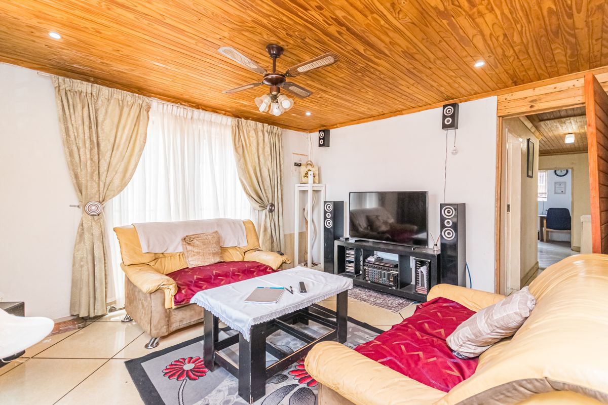 A living room featuring a timber-clad ceiling, ceiling fan, and tiled flooring, providing a functional space with direct access to an adjacent hallway.