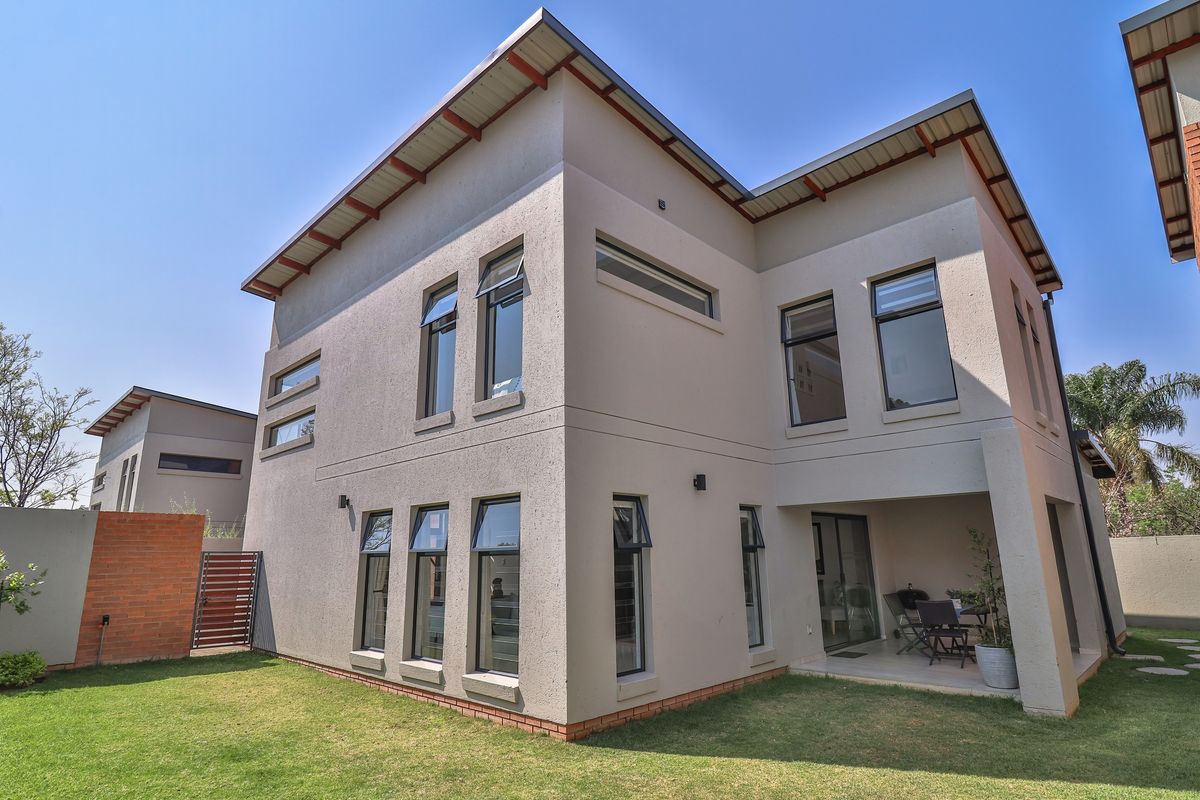 Rear view of a modern double-story townhouse featuring a covered patio, landscaped garden, and contemporary architectural design with large windows.
