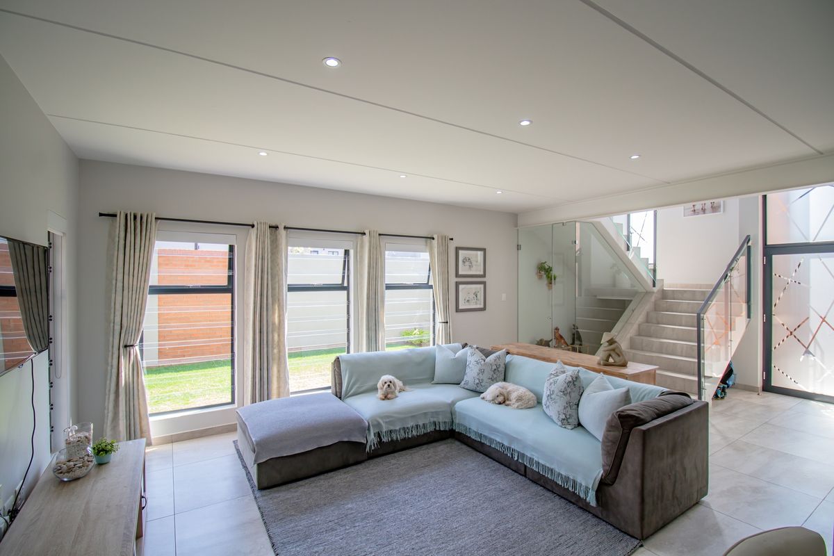 Modern open-plan living area featuring large windows, recessed ceiling lighting, and a glass-enclosed staircase with contemporary finishes.