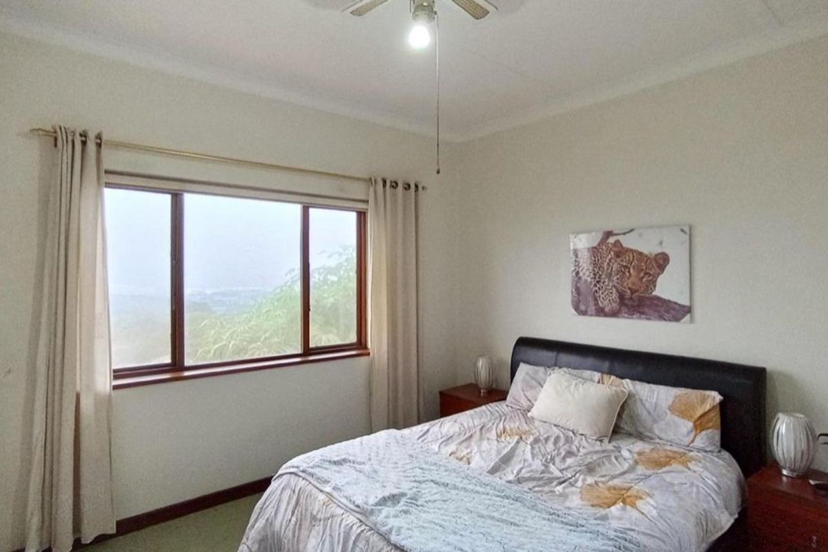 A well-lit bedroom featuring built-in cupboards, a ceiling fan, and large timber-framed windows offering scenic views.