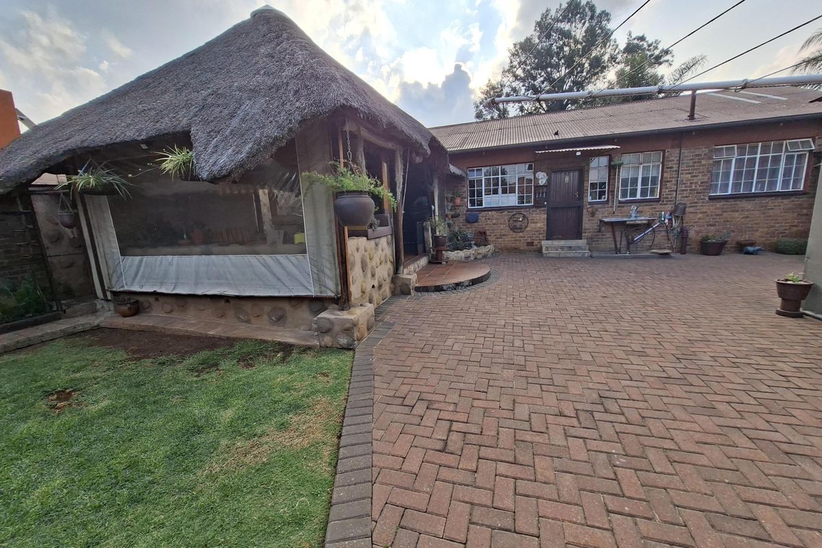 Rear exterior view featuring a thatched lapa area, brick-paved courtyard, and exposed brick house facade with steel-framed windows.