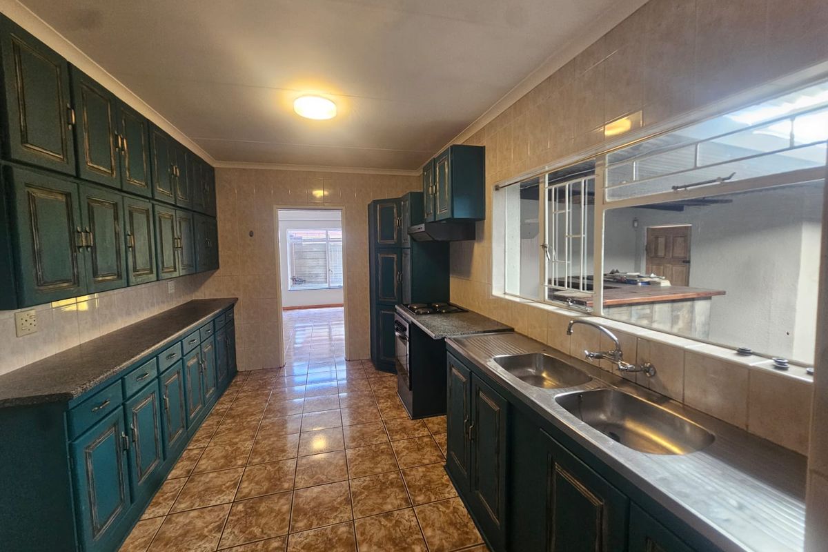 A functional kitchen featuring dark green cabinetry, tiled flooring, a double stainless steel sink, and a built-in stove with an extractor fan.