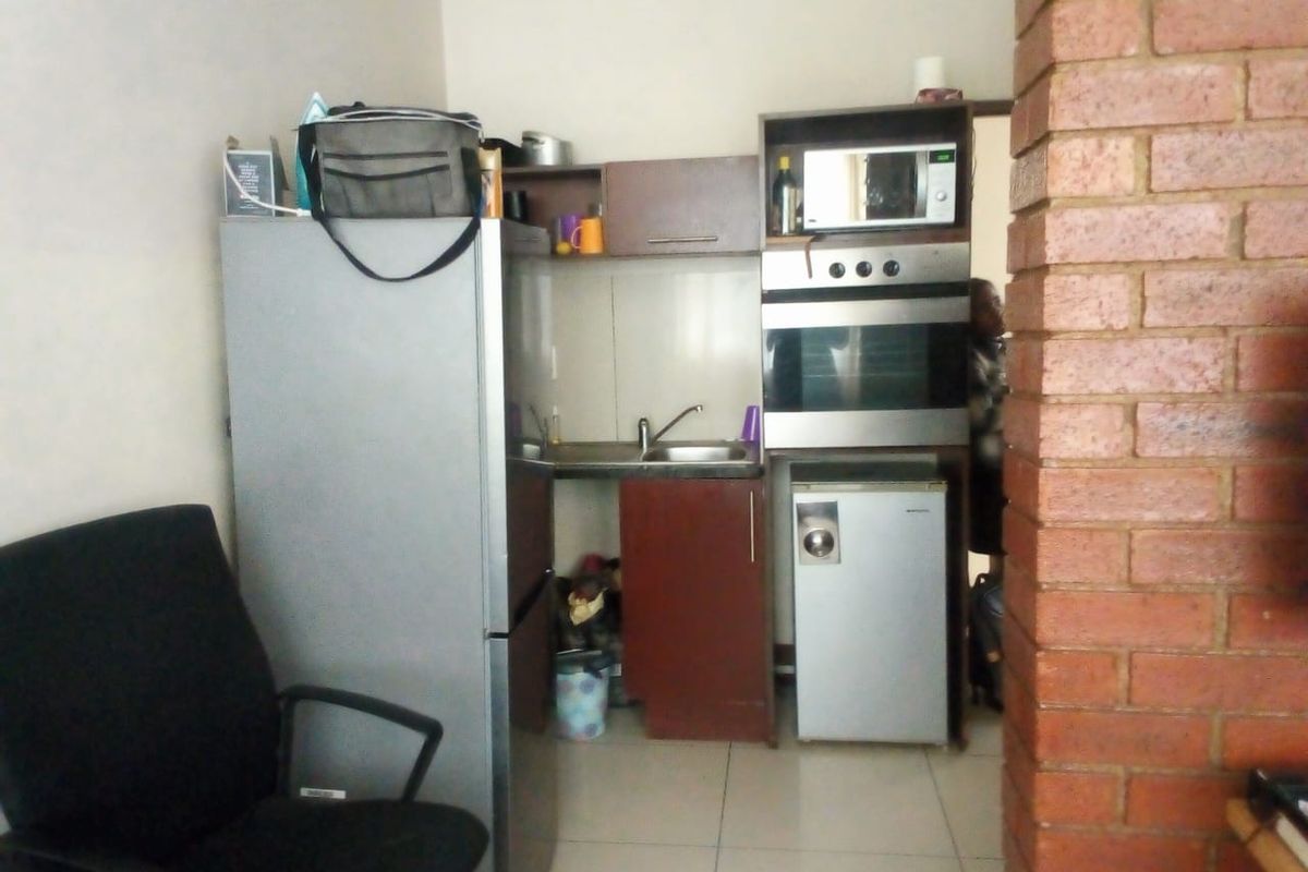 Compact kitchen area featuring built-in oven, microwave, cabinetry, and stainless steel sink, adjacent to an exposed brick feature pillar.