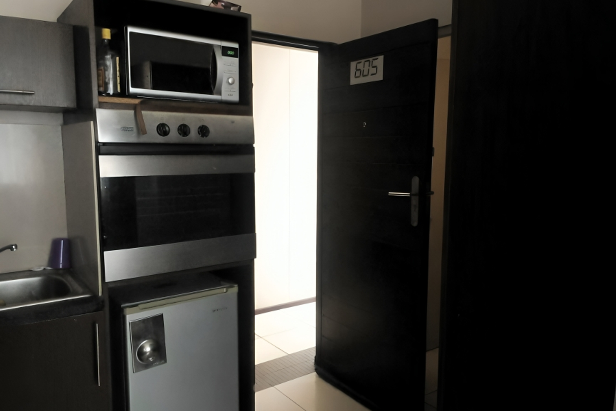 Compact kitchen area featuring built-in oven, microwave, and sink, adjacent to the apartment entrance door.