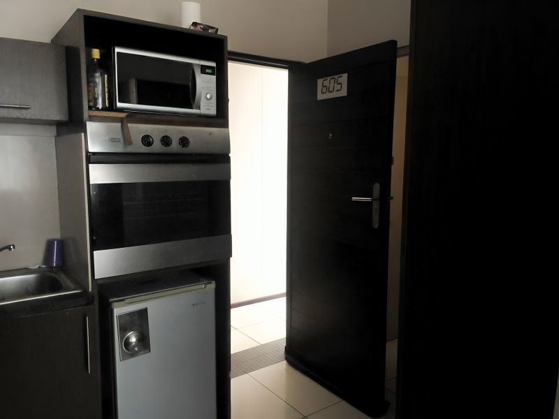 Compact kitchen area featuring built-in oven, microwave, and sink, adjacent to the apartment entrance door.