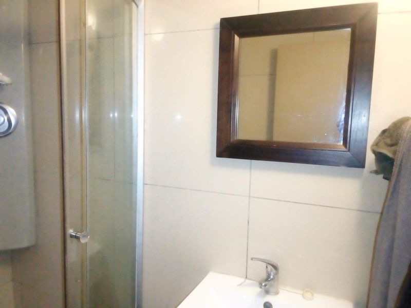 A functional bathroom featuring a glass shower enclosure, a wall-mounted basin with a mixer tap, and tiled wall finishes.